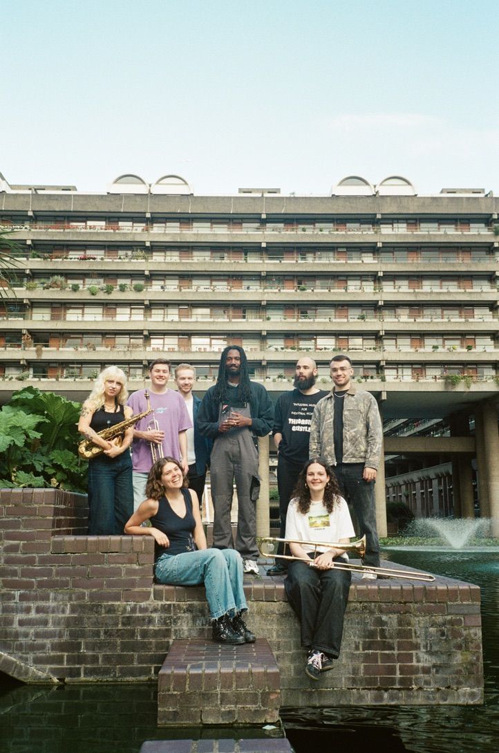 8 musicians holding, some holding instruments, stood in front of the Barbican